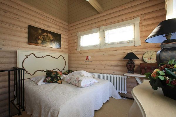 Guļamistabas dizains guļbaļķu mājās neatšķiras: gaiši, mierīgi toņi un vairāki krāsu akcenti