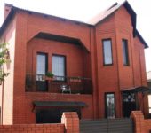 Фасадата на двуетажна къща от червена тухла с характерни черти на модерен стил, но ясен индивидуален характер